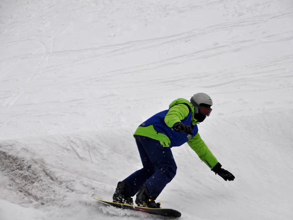 Snowboarder in grüner Jacke in tiefer Hocke.